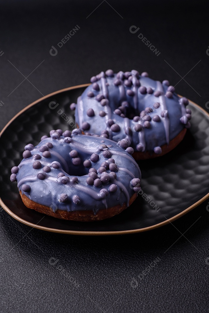 Delicioso donut doce de cor roxa em esmalte e com bolas lilás com recheio de chocolate sobre um fundo escuro de concreto