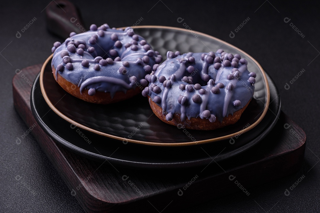 Delicioso donut doce de cor roxa em esmalte e com bolas lilás com recheio de chocolate sobre um fundo escuro de concreto