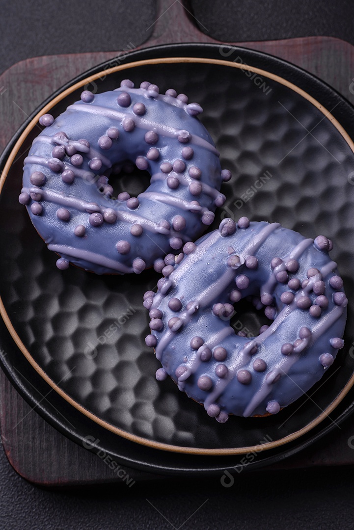 Delicioso donut doce de cor roxa em esmalte e com bolas lilás com recheio de chocolate sobre um fundo escuro de concreto