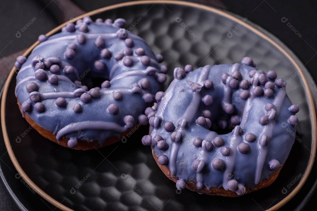 Delicioso donut doce de cor roxa em esmalte e com bolas lilás com recheio de chocolate sobre um fundo escuro de concreto