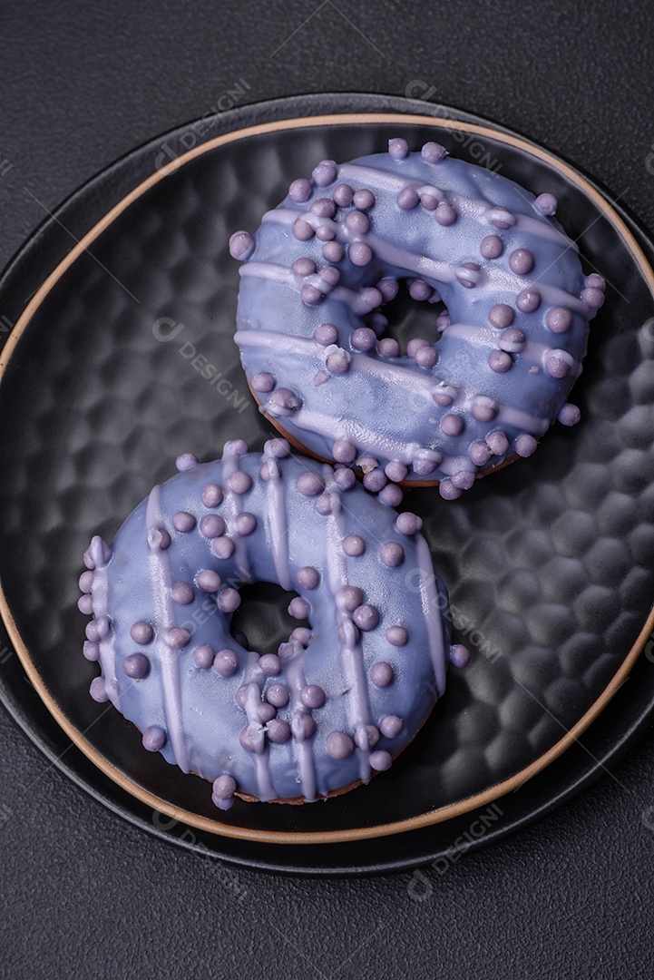 Delicioso donut doce de cor roxa em esmalte e com bolas lilás com recheio de chocolate sobre um fundo escuro de concreto