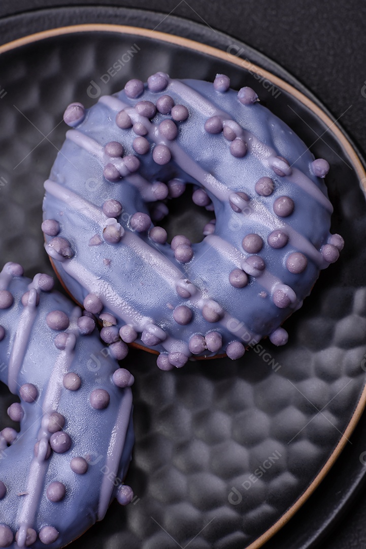 Delicioso donut doce de cor roxa em esmalte e com bolas lilás com recheio de chocolate sobre um fundo escuro de concreto