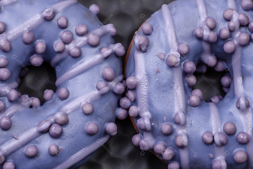 Delicioso donut doce de cor roxa em esmalte e com bolas lilás com recheio de chocolate sobre um fundo escuro de concreto