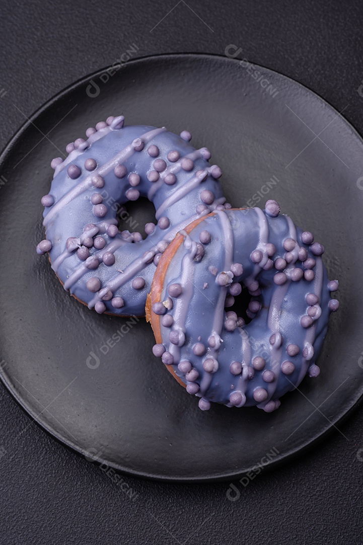 Delicioso donut doce de cor roxa em esmalte e com bolas lilás com recheio de chocolate sobre um fundo escuro de concreto