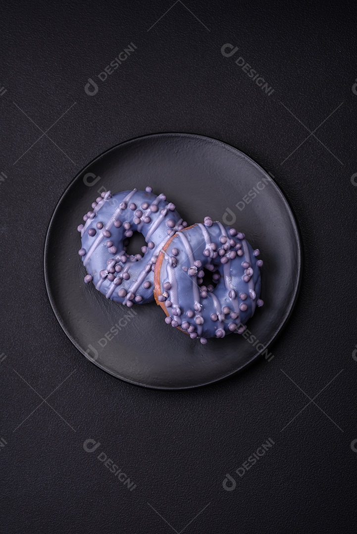 Delicioso donut doce de cor roxa em esmalte e com bolas lilás com recheio de chocolate sobre um fundo escuro de concreto