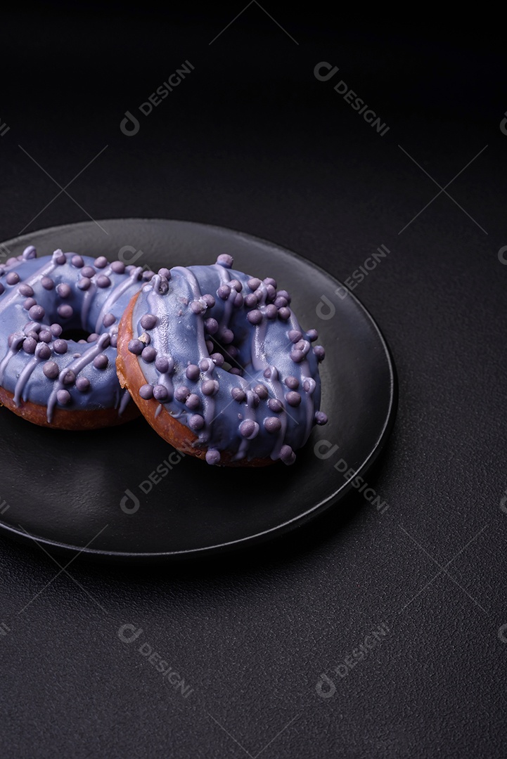 Delicioso donut doce de cor roxa em esmalte e com bolas lilás com recheio de chocolate sobre um fundo escuro de concreto