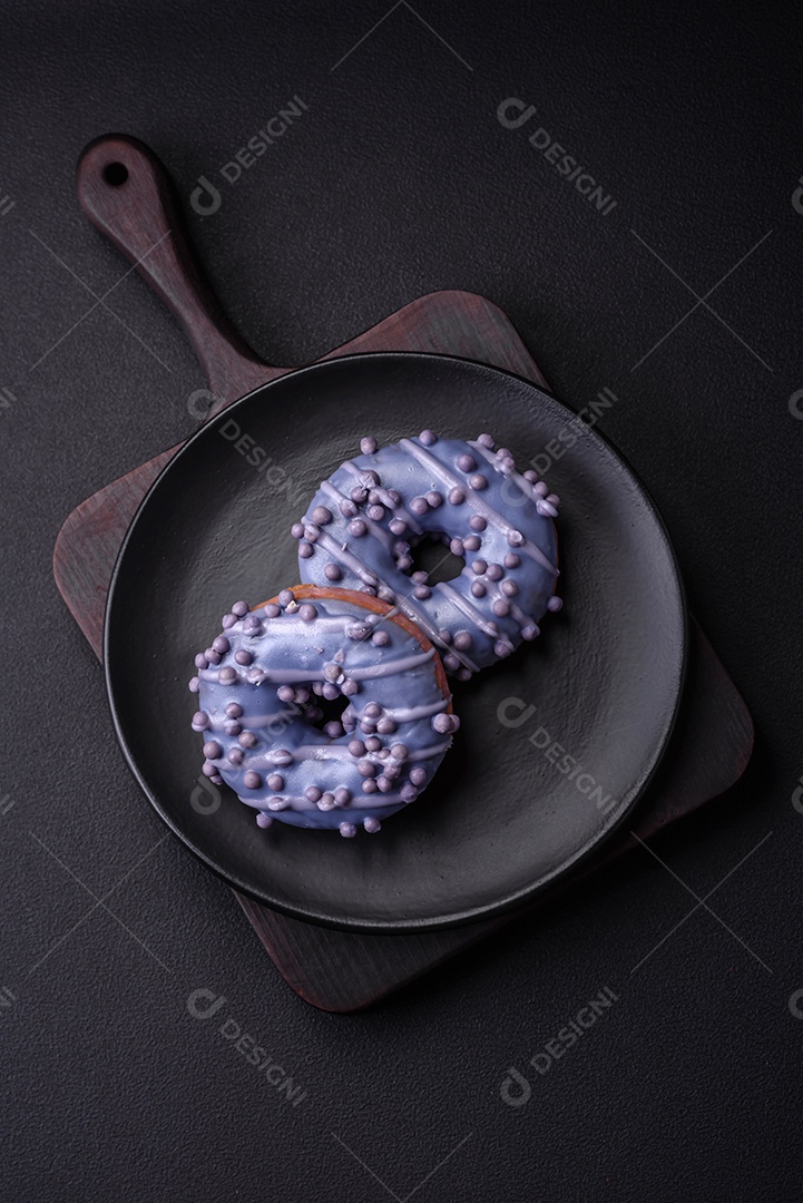 Delicioso donut doce de cor roxa em esmalte e com bolas lilás com recheio de chocolate sobre um fundo escuro de concreto
