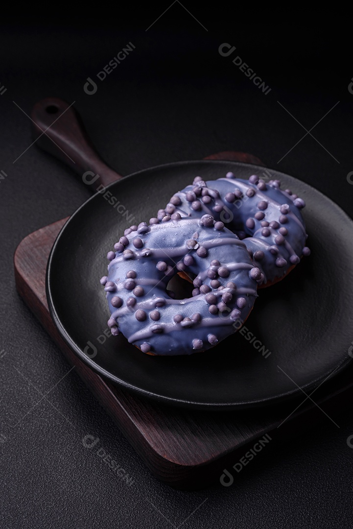 Delicioso donut doce de cor roxa em esmalte e com bolas lilás com recheio de chocolate sobre um fundo escuro de concreto