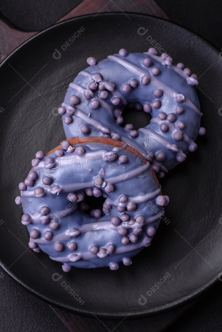 Delicioso donut doce de cor roxa em esmalte e com bolas lilás com recheio de chocolate sobre um fundo escuro de concreto