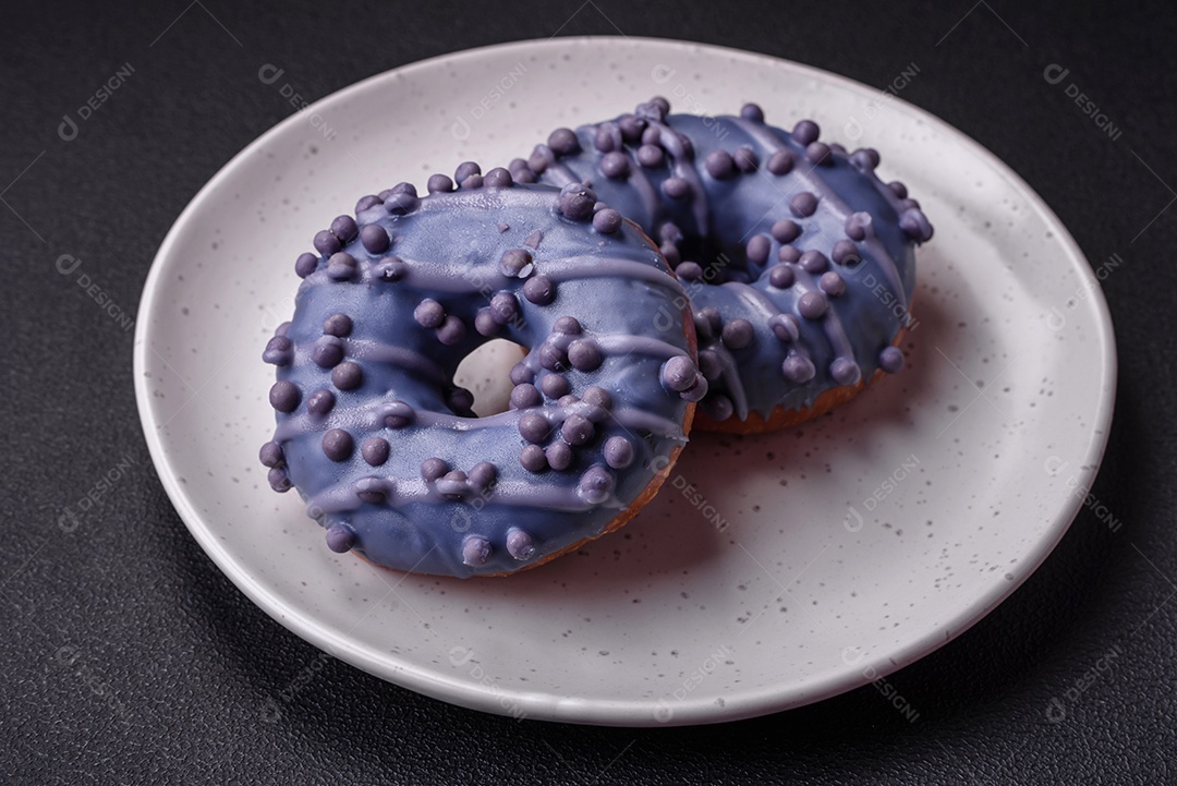 Delicioso donut doce de cor roxa em esmalte e com bolas lilás com recheio de chocolate sobre um fundo escuro de concreto