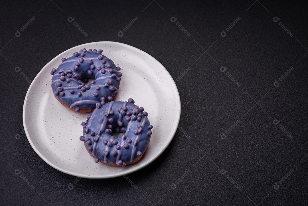 Delicioso donut doce de cor roxa em esmalte e com bolas lilás com recheio de chocolate sobre um fundo escuro de concreto
