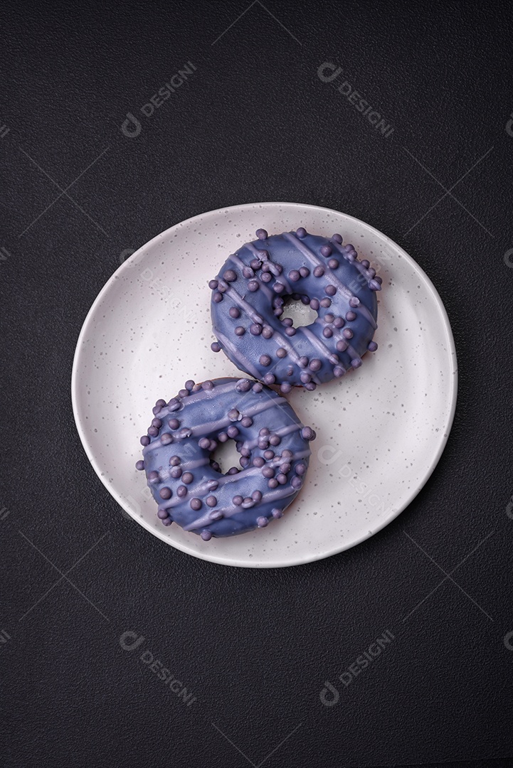 Delicioso donut doce de cor roxa em esmalte e com bolas lilás com recheio de chocolate sobre um fundo escuro de concreto