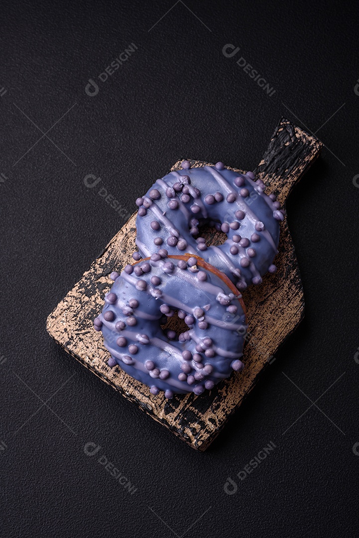 Delicioso donut doce de cor roxa em esmalte e com bolas lilás com recheio de chocolate sobre um fundo escuro de concreto