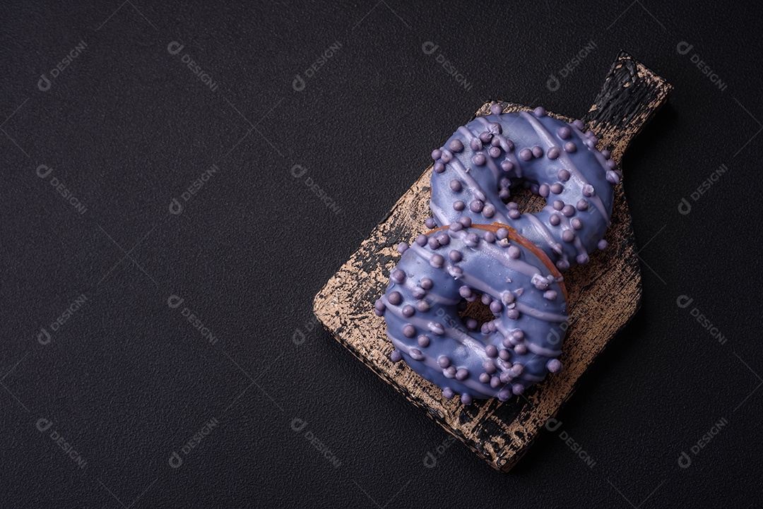 Delicioso donut doce de cor roxa em esmalte e com bolas lilás com recheio de chocolate sobre um fundo escuro de concreto