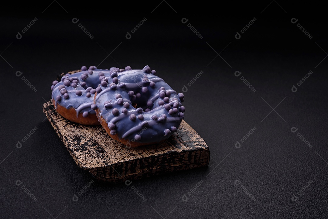 Delicioso donut doce de cor roxa em esmalte e com bolas lilás com recheio de chocolate sobre um fundo escuro de concreto