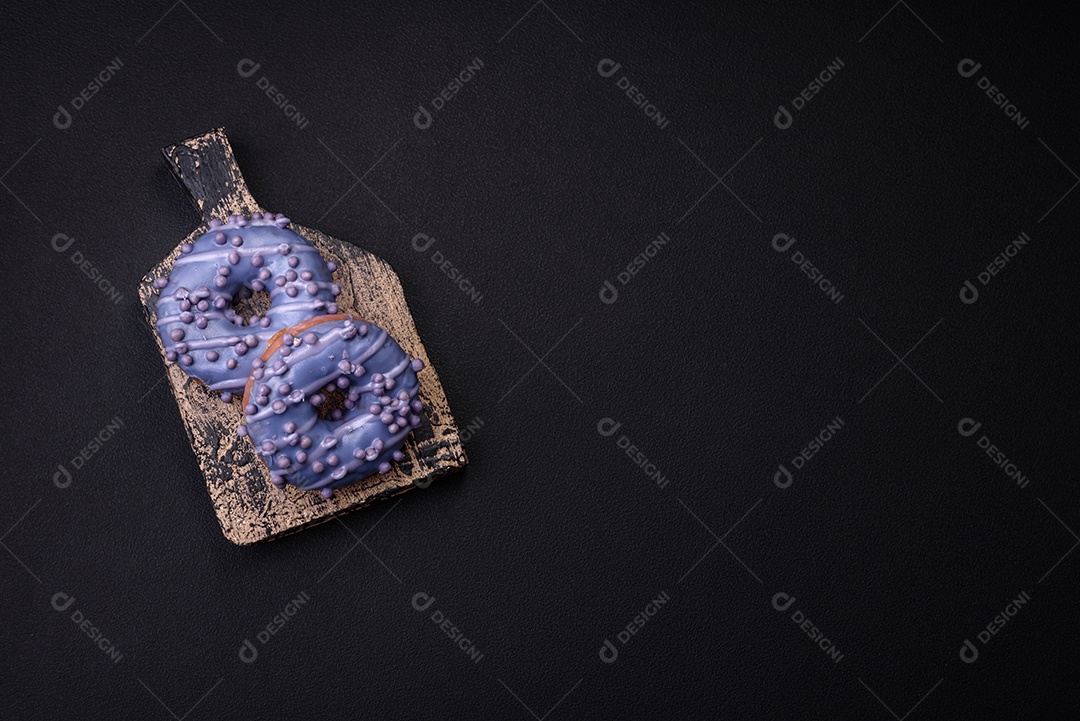 Delicioso donut doce de cor roxa em esmalte e com bolas lilás com recheio de chocolate sobre um fundo escuro de concreto