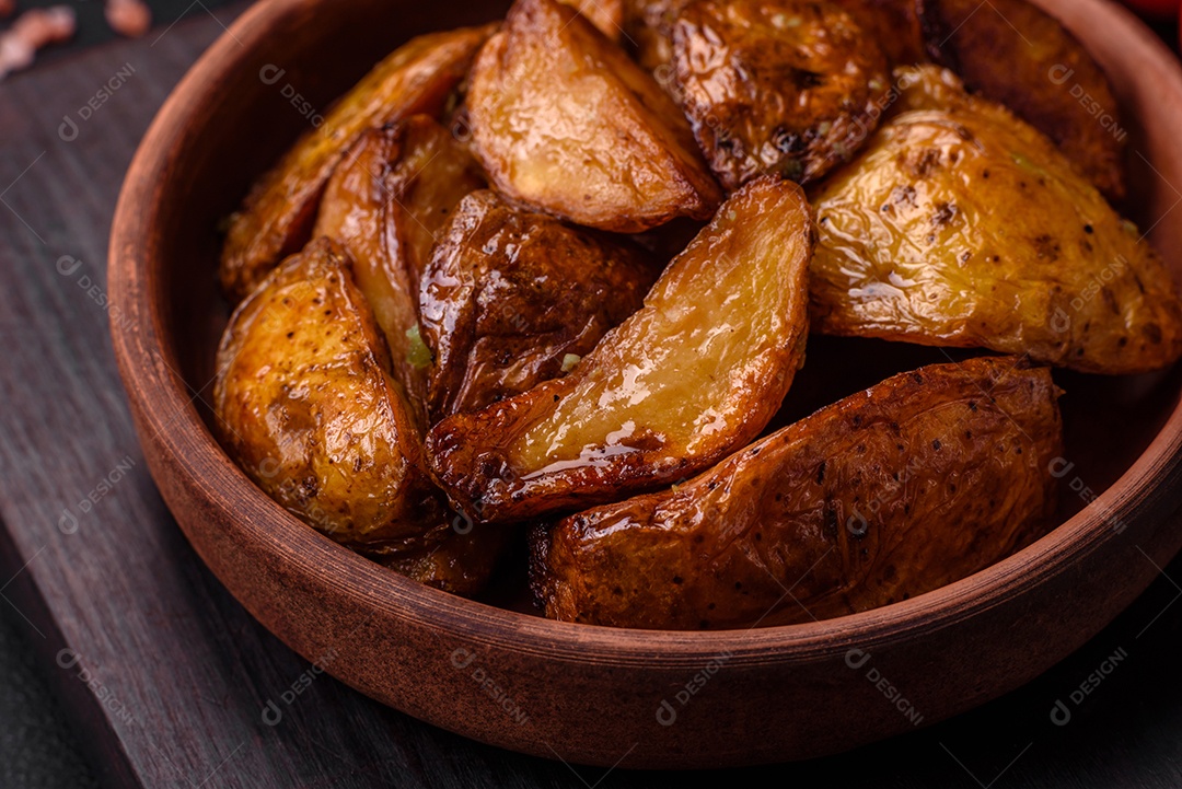 Deliciosas fatias de batata grelhada com alho, especiarias e ervas sobre um fundo escuro de concreto