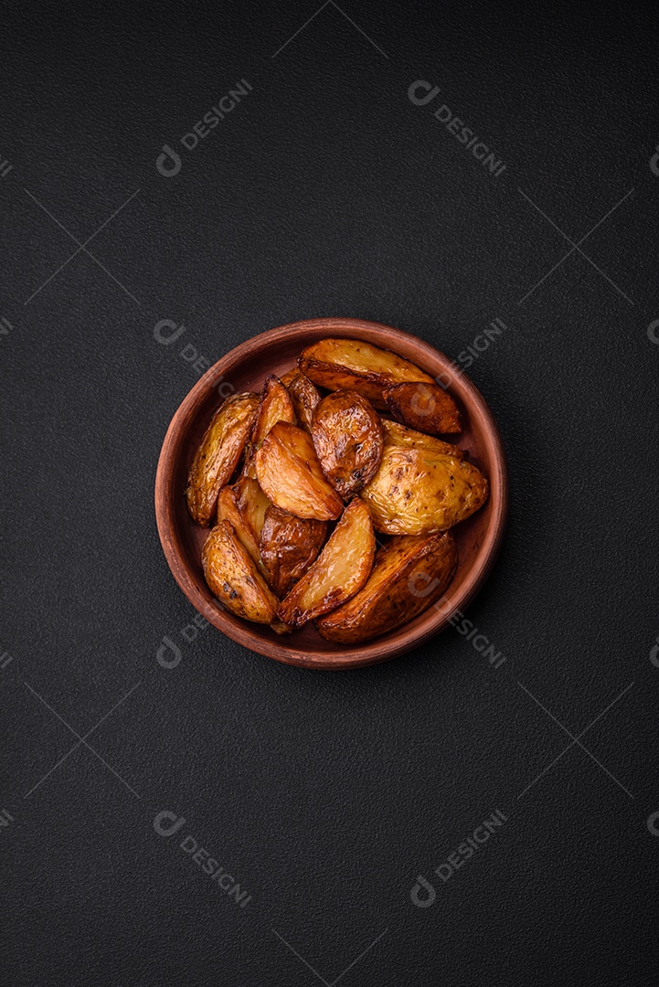 Deliciosas fatias de batata grelhada com alho, especiarias e ervas sobre um fundo escuro de concreto