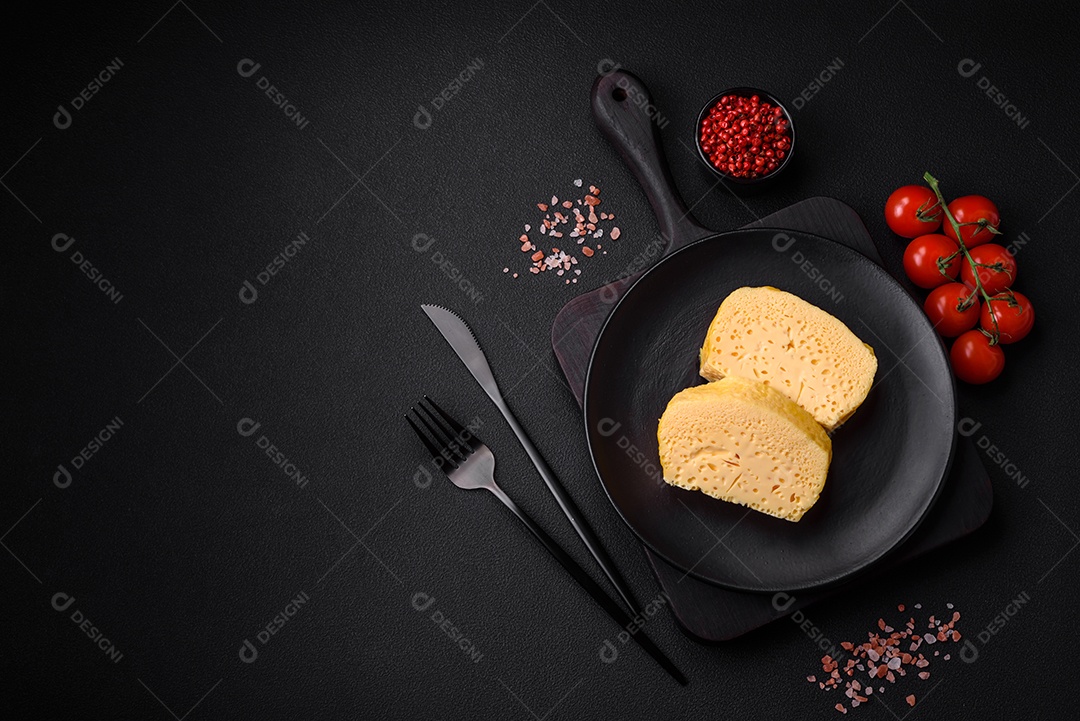 Delicioso queijo amarelo poroso cortado em pedaços grandes numa placa cerâmica sobre um fundo escuro de concreto