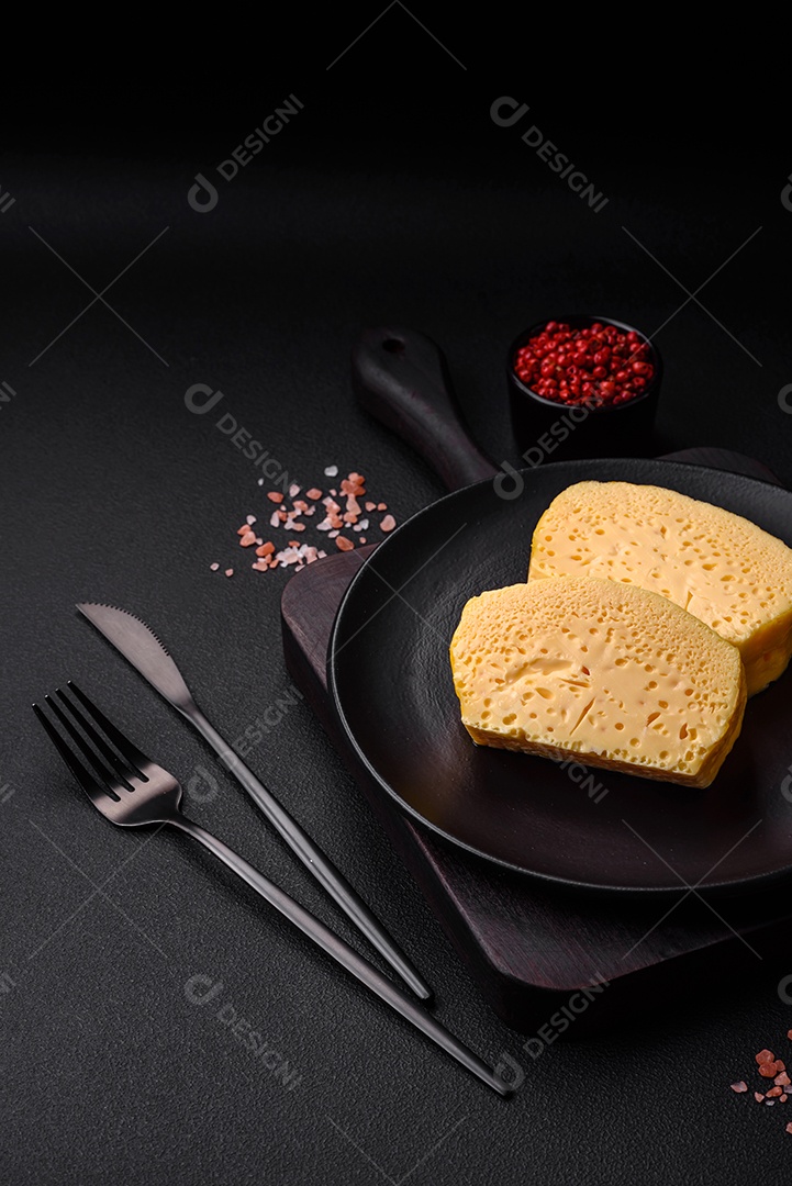 Delicioso queijo amarelo poroso cortado em pedaços grandes numa placa cerâmica sobre um fundo escuro de concreto