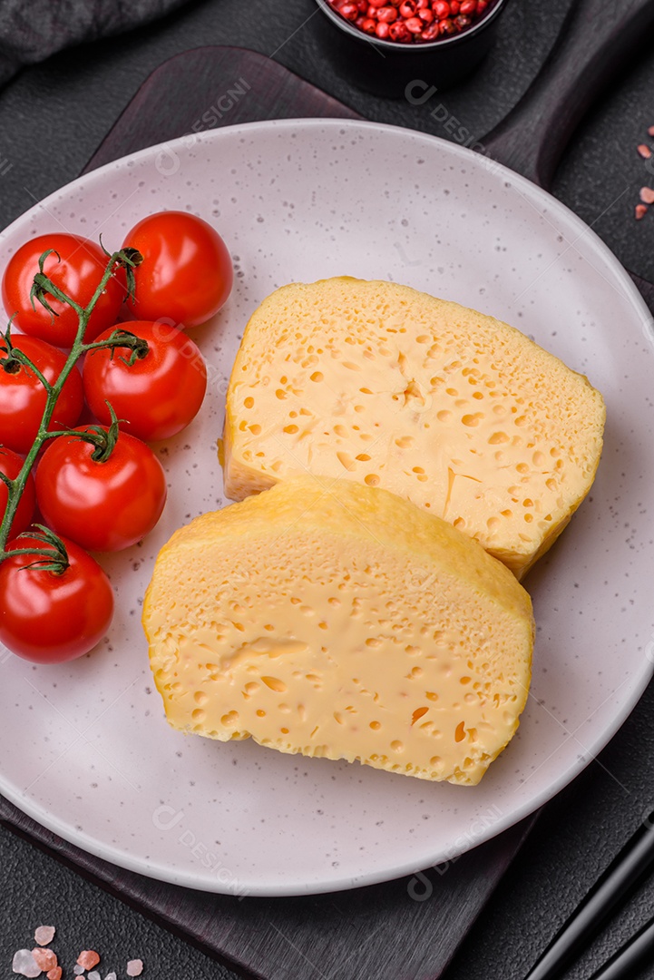 Delicioso queijo amarelo poroso cortado em pedaços grandes numa placa cerâmica sobre um fundo escuro de concreto