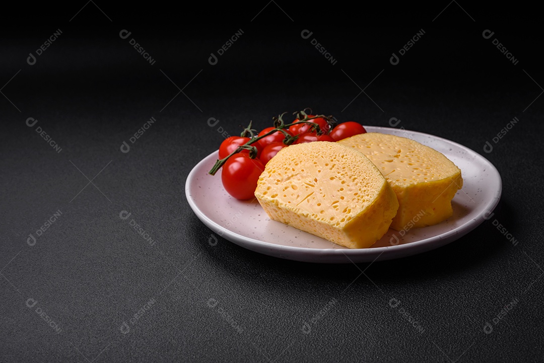 Delicioso queijo amarelo poroso cortado em pedaços grandes numa placa cerâmica sobre um fundo escuro de concreto