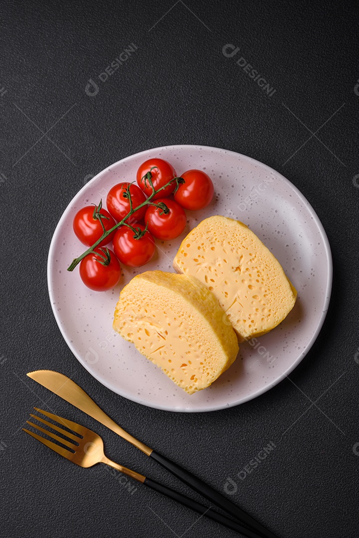 Delicioso queijo amarelo poroso cortado em pedaços grandes numa placa cerâmica sobre um fundo escuro de concreto