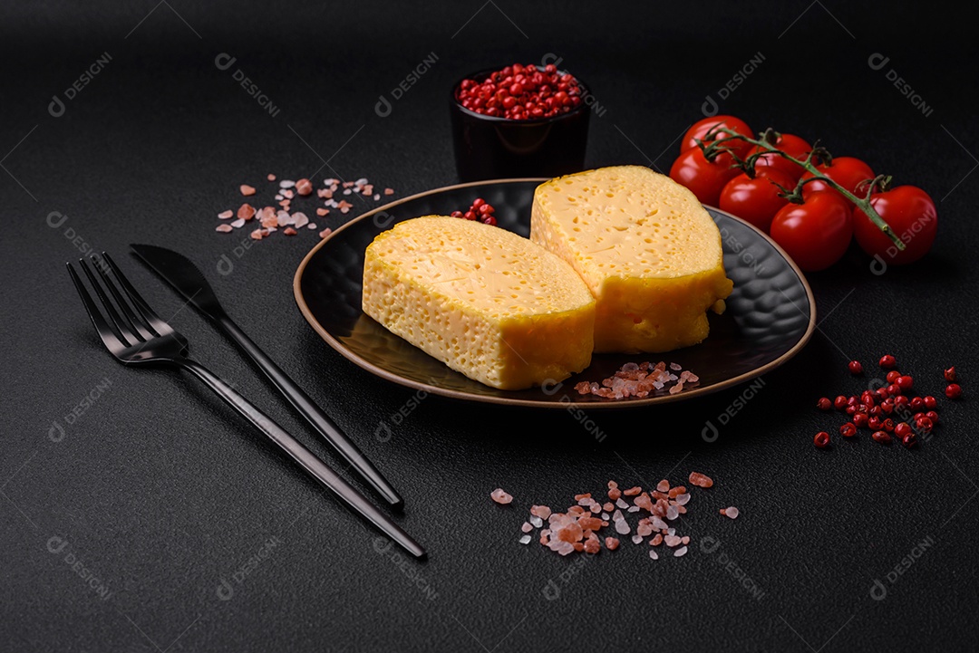 Delicioso queijo amarelo poroso cortado em pedaços grandes numa placa cerâmica sobre um fundo escuro de concreto