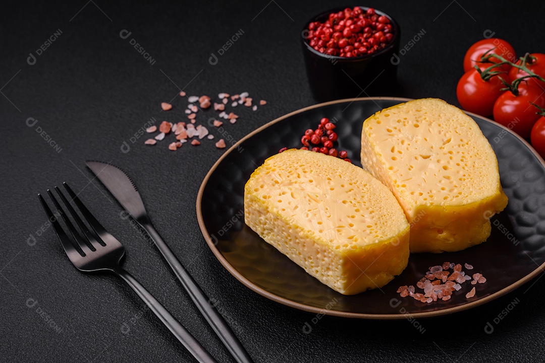 Delicioso queijo amarelo poroso cortado em pedaços grandes numa placa cerâmica sobre um fundo escuro de concreto
