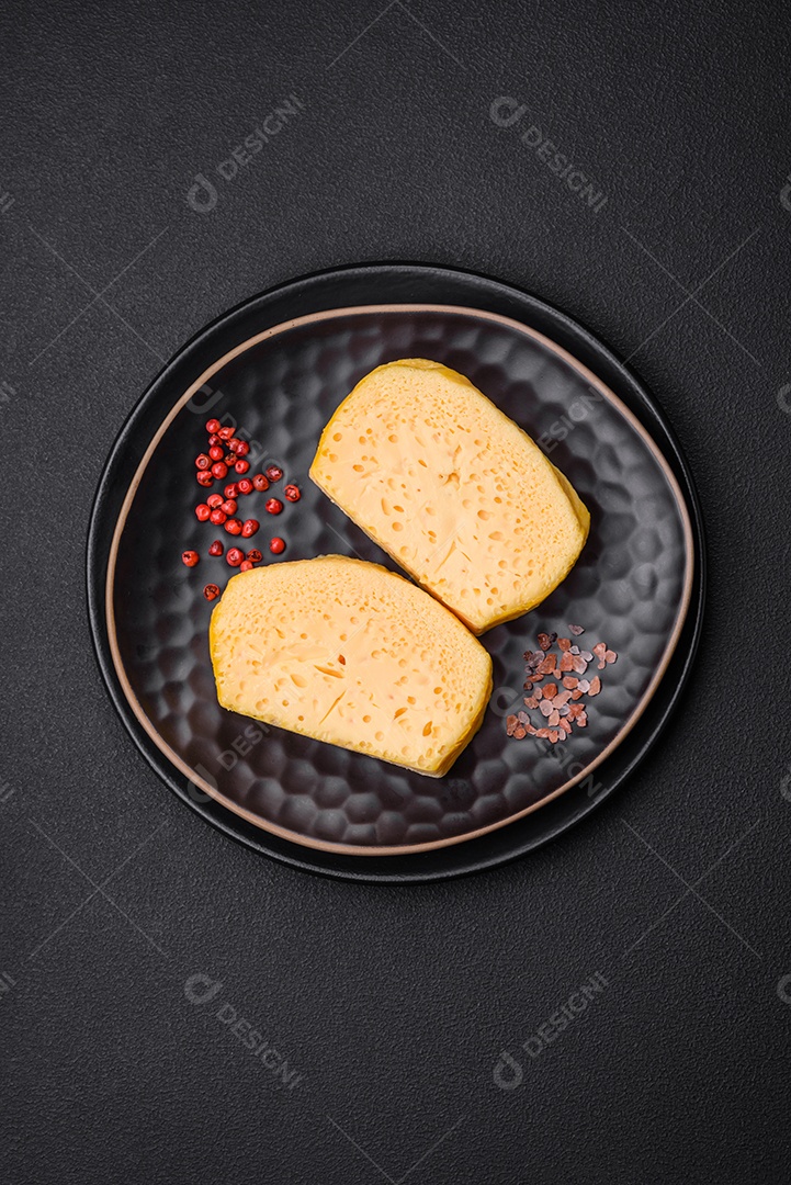 Delicioso queijo amarelo poroso cortado em pedaços grandes numa placa cerâmica sobre um fundo escuro de concreto