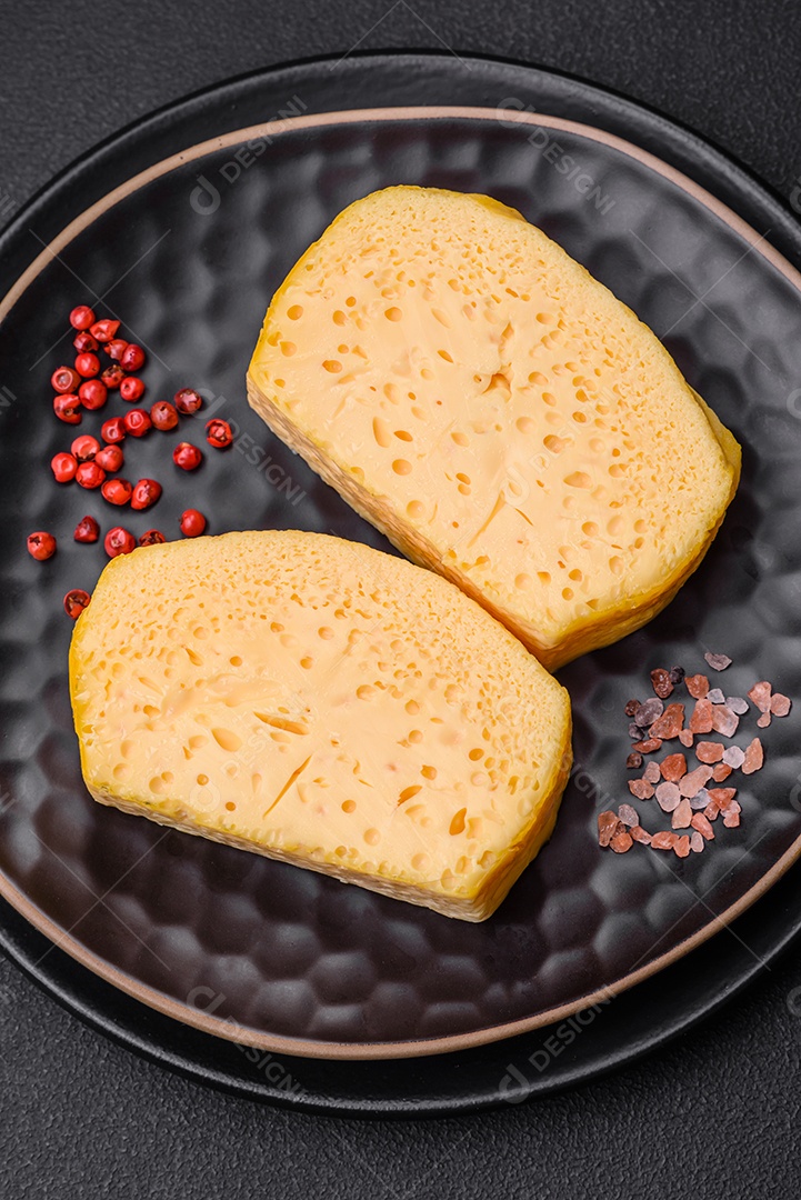 Delicioso queijo amarelo poroso cortado em pedaços grandes numa placa cerâmica sobre um fundo escuro de concreto