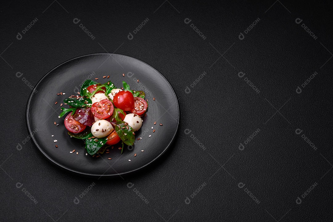 Deliciosa salada fresca com queijo mussarela, tomate cereja, ervas, sal e especiarias sobre um fundo escuro de concreto