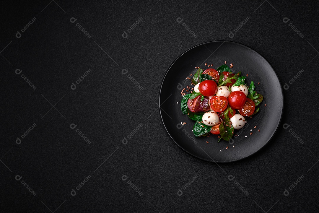 Deliciosa salada fresca com queijo mussarela, tomate cereja, ervas, sal e especiarias sobre um fundo escuro de concreto