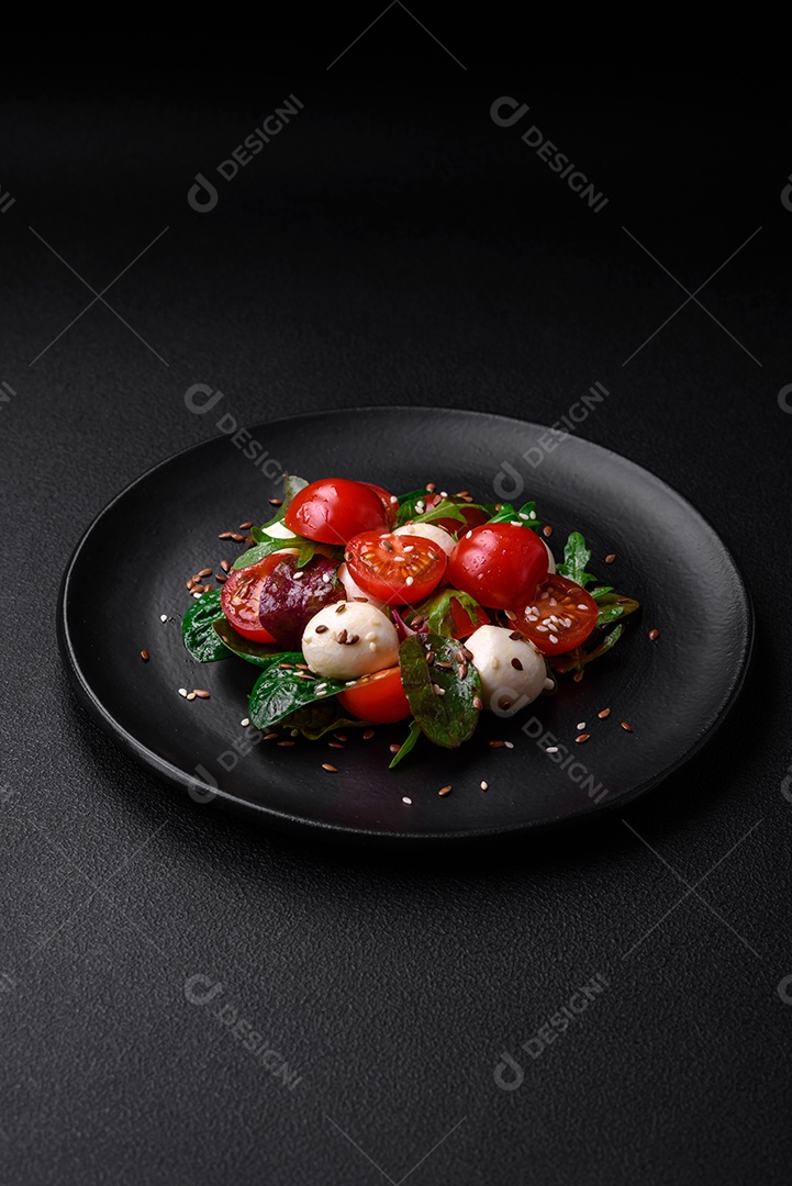 Deliciosa salada fresca com queijo mussarela, tomate cereja, ervas, sal e especiarias sobre um fundo escuro de concreto