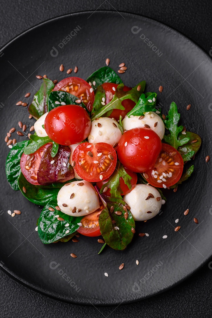 Deliciosa salada fresca com queijo mussarela, tomate cereja, ervas, sal e especiarias sobre um fundo escuro de concreto