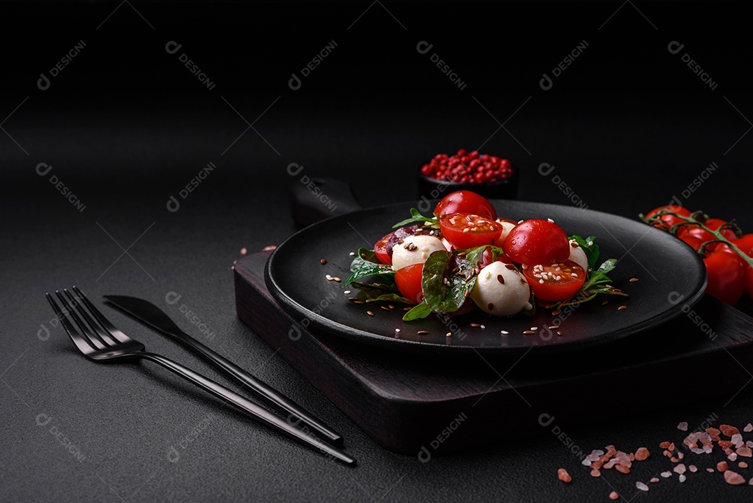 Deliciosa salada fresca com queijo mussarela, tomate cereja, ervas, sal e especiarias sobre um fundo escuro de concreto