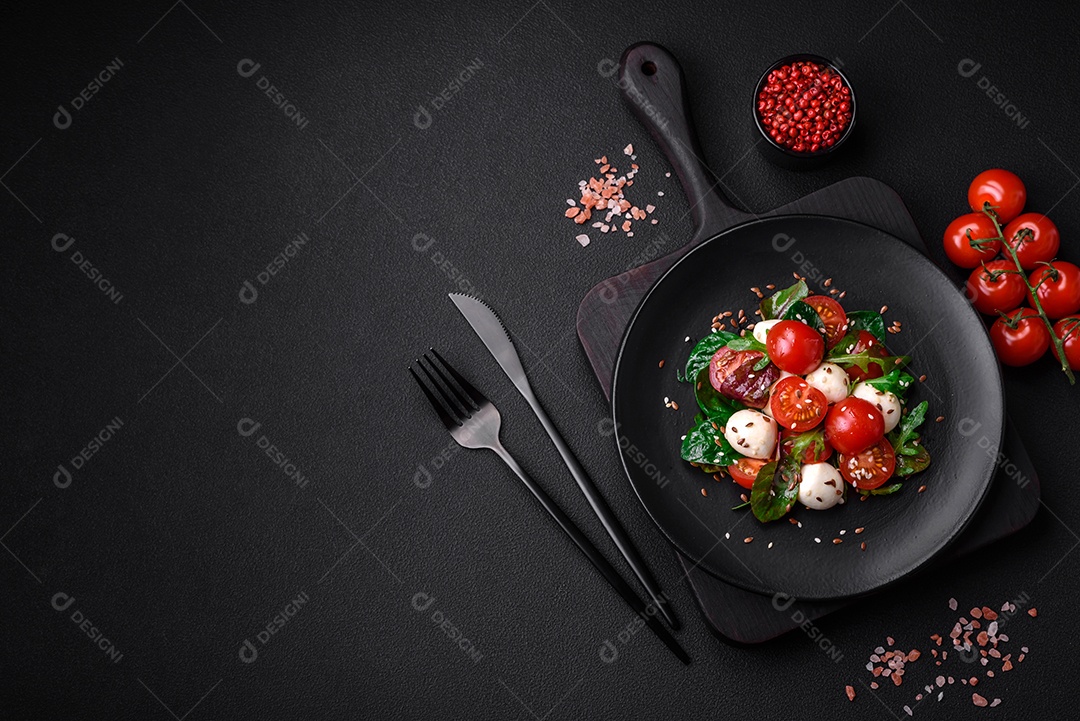 Deliciosa salada fresca com queijo mussarela, tomate cereja, ervas, sal e especiarias sobre um fundo escuro de concreto