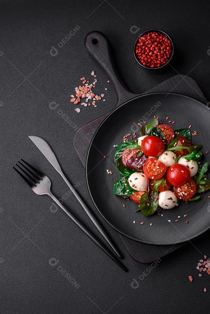 Deliciosa salada fresca com queijo mussarela, tomate cereja, ervas, sal e especiarias sobre um fundo escuro de concreto