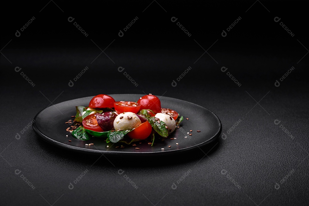 Deliciosa salada fresca com queijo mussarela, tomate cereja, ervas, sal e especiarias sobre um fundo escuro de concreto