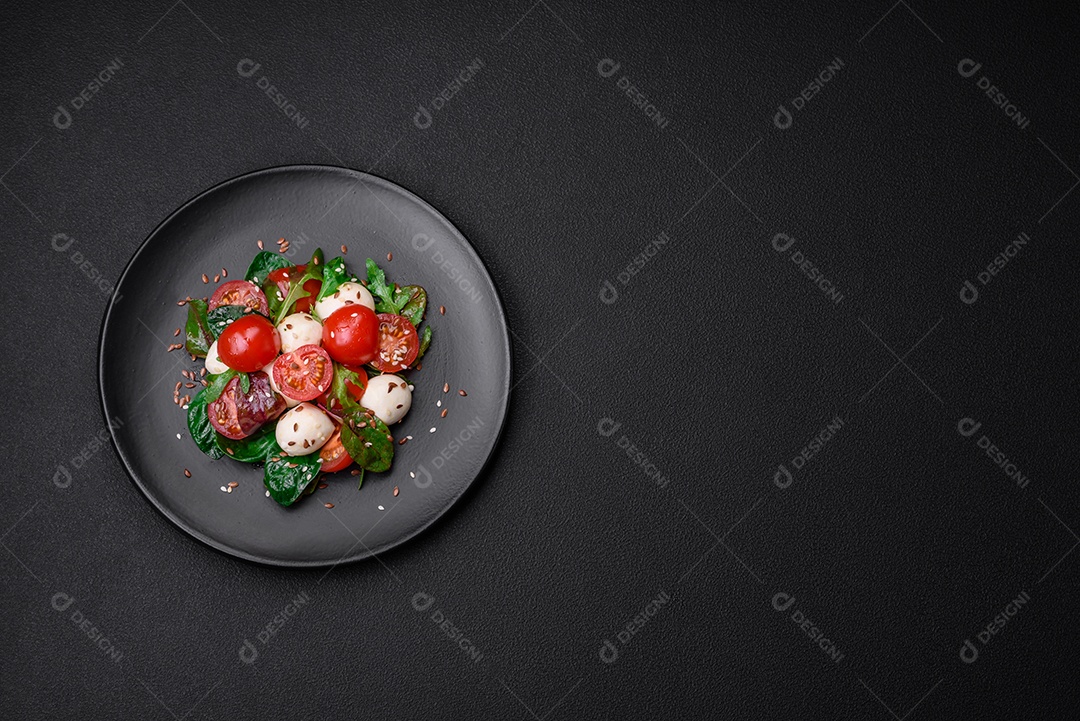 Deliciosa salada fresca com queijo mussarela, tomate cereja, ervas, sal e especiarias sobre um fundo escuro de concreto