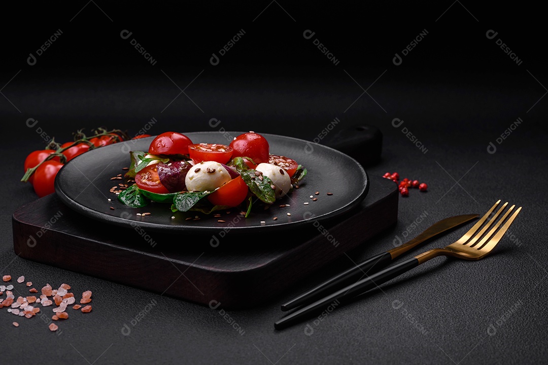 Deliciosa salada fresca com queijo mussarela, tomate cereja, ervas, sal e especiarias sobre um fundo escuro de concreto