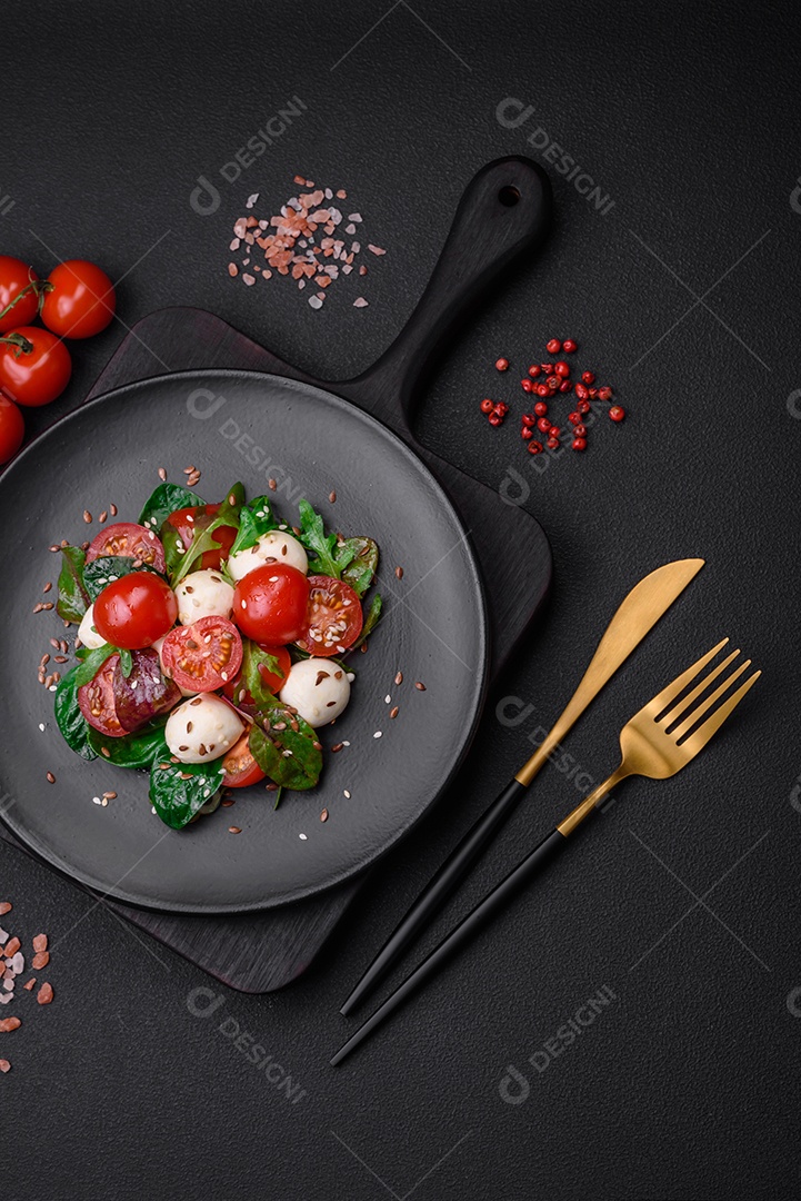 Deliciosa salada fresca com queijo mussarela, tomate cereja, ervas, sal e especiarias sobre um fundo escuro de concreto