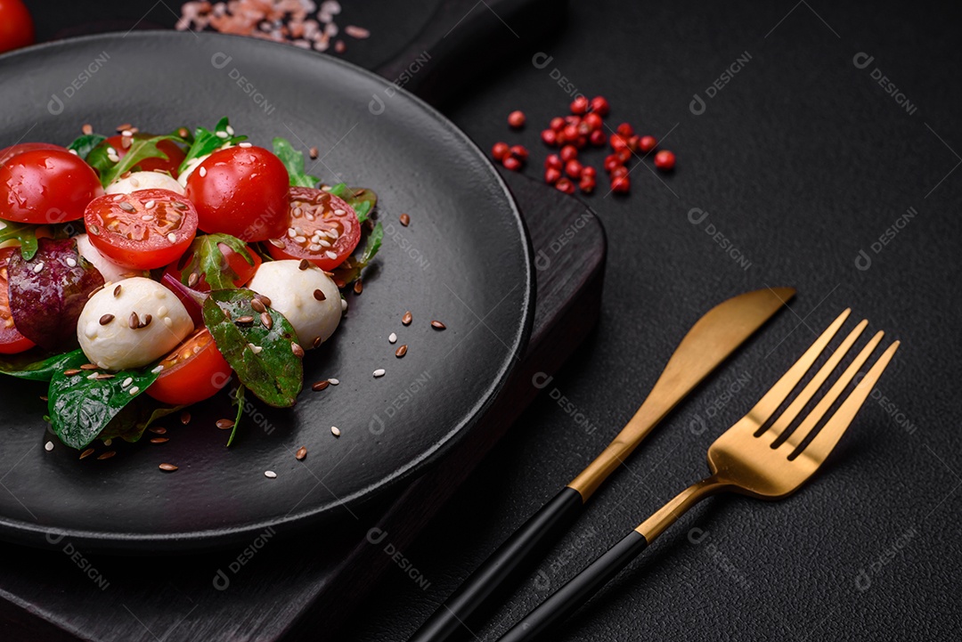 Deliciosa salada fresca com queijo mussarela, tomate cereja, ervas, sal e especiarias sobre um fundo escuro de concreto