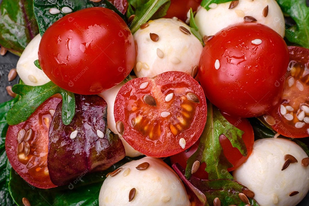 Deliciosa salada fresca com queijo mussarela, tomate cereja, ervas, sal e especiarias sobre um fundo escuro de concreto