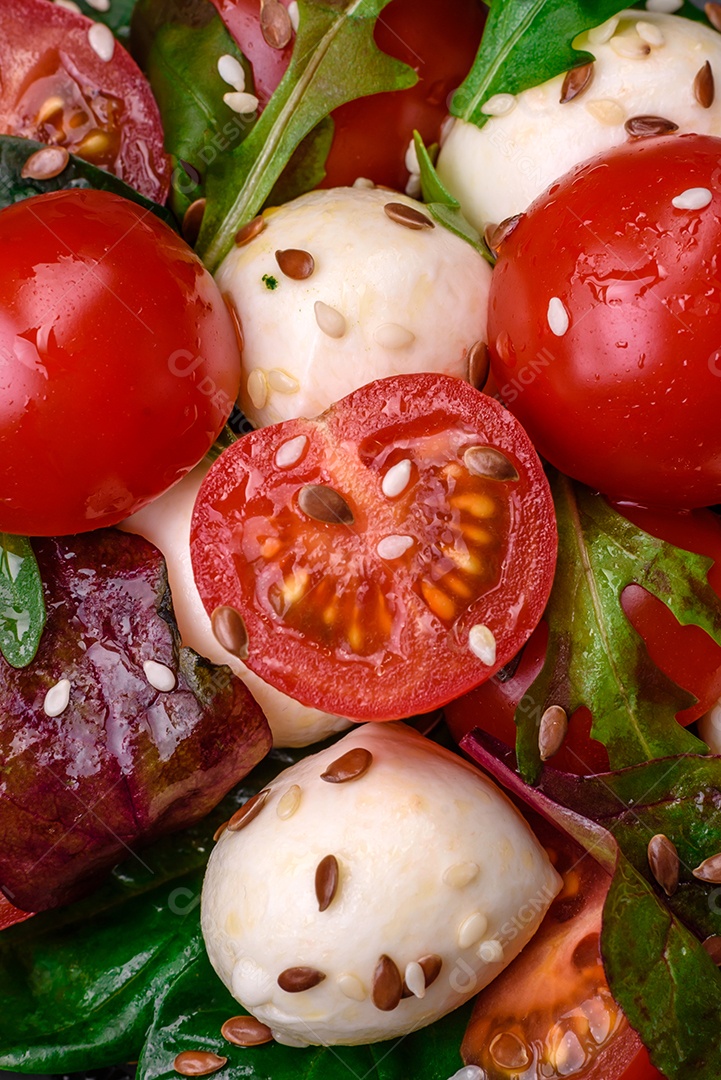 Deliciosa salada fresca com queijo mussarela, tomate cereja, ervas, sal e especiarias sobre um fundo escuro de concreto