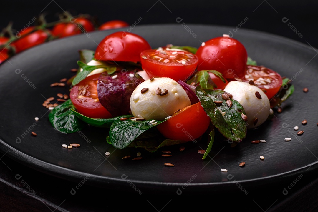 Deliciosa salada fresca com queijo mussarela, tomate cereja, ervas, sal e especiarias sobre um fundo escuro de concreto