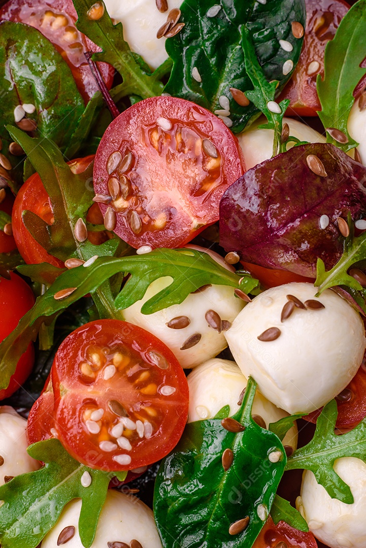 Deliciosa salada fresca com queijo mussarela, tomate cereja, ervas, sal e especiarias sobre um fundo escuro de concreto