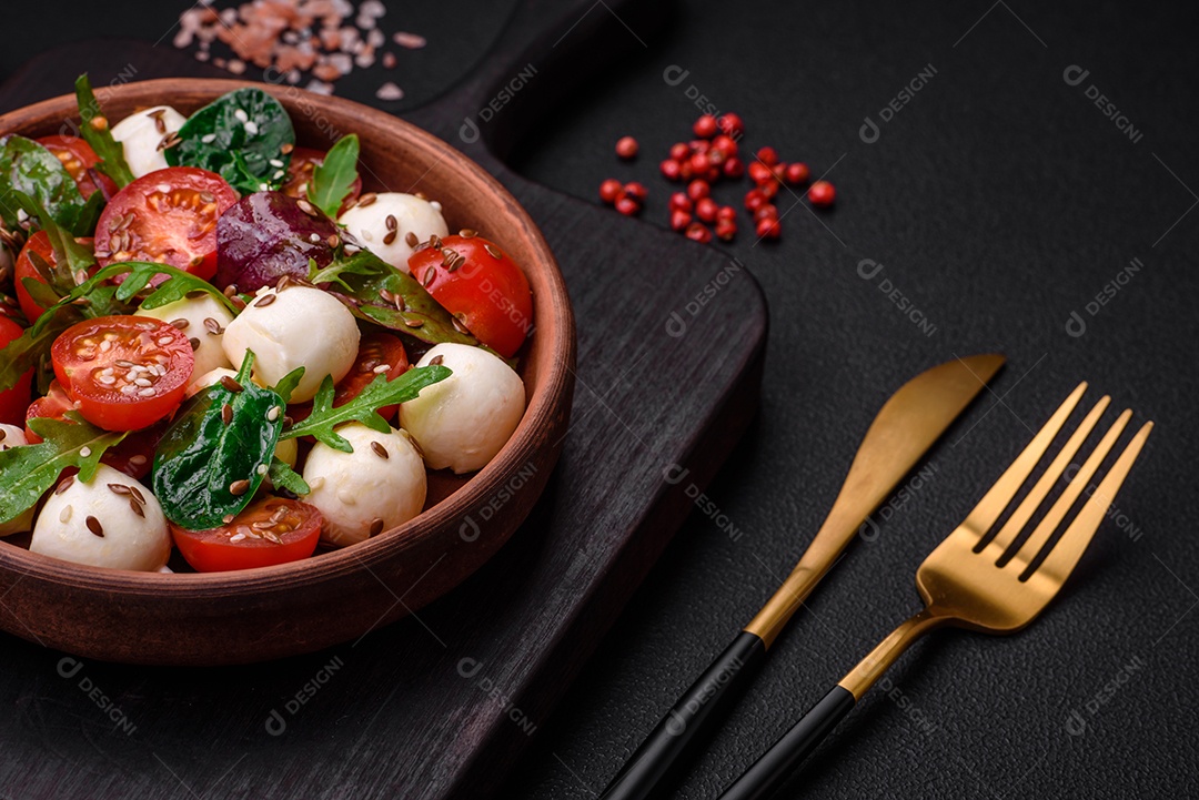 Deliciosa salada fresca com queijo mussarela, tomate cereja, ervas, sal e especiarias sobre um fundo escuro de concreto