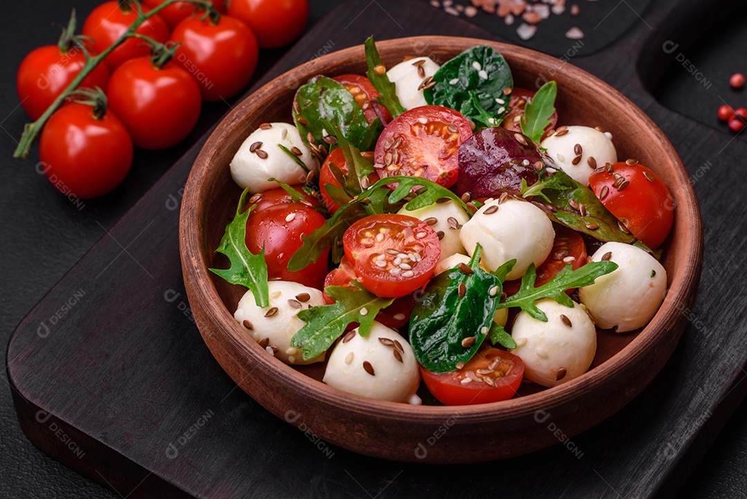 Deliciosa salada fresca com queijo mussarela, tomate cereja, ervas, sal e especiarias sobre um fundo escuro de concreto