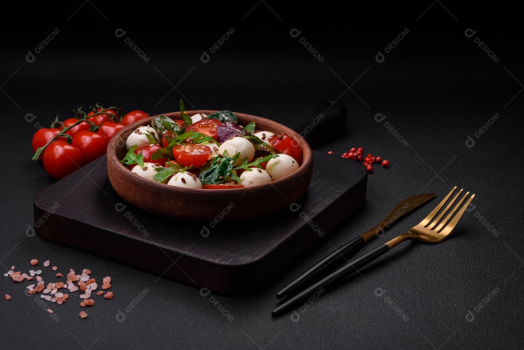 Deliciosa salada fresca com queijo mussarela, tomate cereja, ervas, sal e especiarias sobre um fundo escuro de concreto